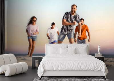 Happy friends playing football on beach during sunset, low angle view Wall mural