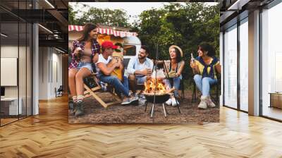 Happy friends sitting near bonfire. Camping season Wall mural