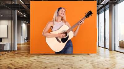 Happy hippie woman playing guitar on orange background Wall mural