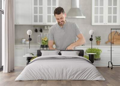 Happy man cutting celery for delicious smoothie at white marble table in kitchen Wall mural