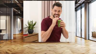 Happy man drinking delicious fresh smoothie at home Wall mural