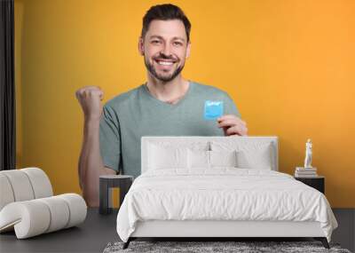 Happy man holding condom on orange background Wall mural