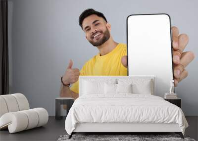 Happy man holding smartphone with empty screen and showing thumbs up on grey background, space for text Wall mural