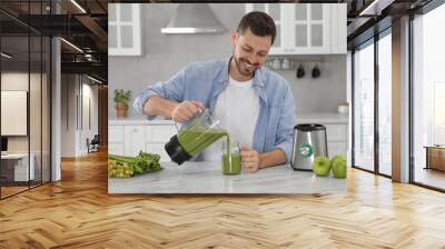 Happy man pouring delicious smoothie into glass at white marble table in kitchen Wall mural