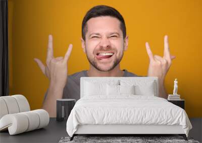 Happy man showing his tongue and rock gesture on orange background Wall mural