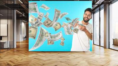 Happy man throwing money on light blue background. Dollar bills flying away from him Wall mural