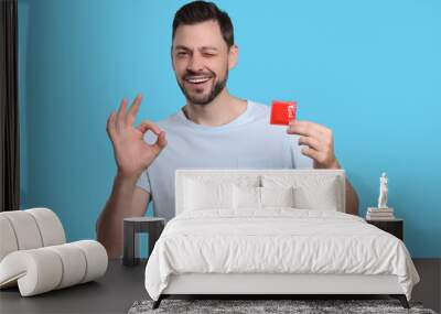 Happy man with condom showing ok gesture on light blue background Wall mural