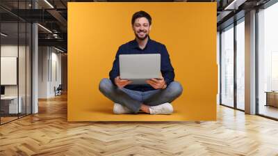 Happy man with laptop sitting on yellow background Wall mural