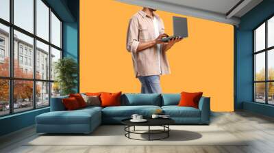 Happy man with laptop walking on orange background Wall mural