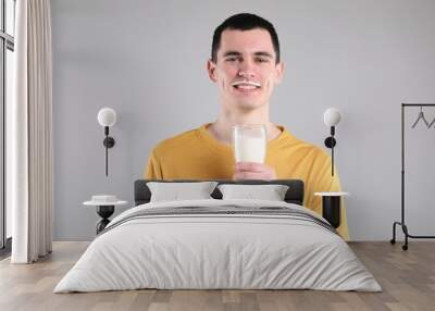 Happy man with milk mustache holding glass of tasty dairy drink on gray background Wall mural