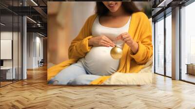 Happy pregnant woman with Christmas ball in armchair at home. Expecting baby Wall mural