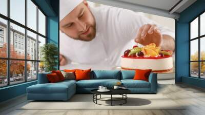 Happy professional confectioner decorating delicious cake at table in kitchen Wall mural