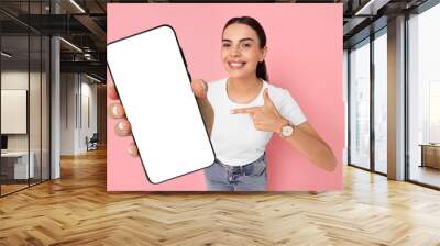 Happy woman pointing at mobile phone with blank screen on pink background. Mockup for design Wall mural