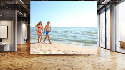 Happy young couple in beachwear walking together on seashore Wall mural