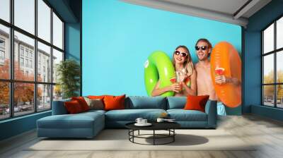 Happy young couple in beachwear with inflatable rings and cocktails on color background. Space for text Wall mural