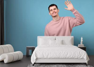 Happy young man waving on light blue background, space for text Wall mural