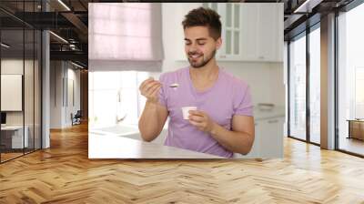 Happy young man with tasty yogurt at table in kitchen Wall mural