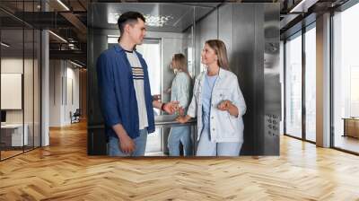 Happy young people talking in modern elevator Wall mural