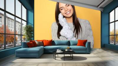 Happy young woman wearing warm sweater and mittens on yellow background Wall mural