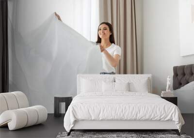 Happy young woman with clean bedsheet in room. Laundry day Wall mural