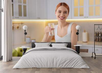 Happy young woman with glass of water and pills at table in kitchen. Weight loss Wall mural