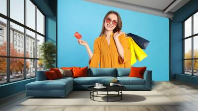 Happy young woman with shopping bags and credit card on light blue background. Big sale Wall mural