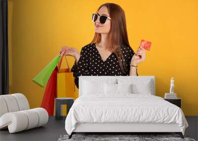 Happy young woman with shopping bags and credit card on yellow background. Big sale Wall mural