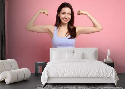 Happy young woman with slim body showing her muscles on pink background Wall mural