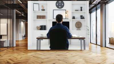 Home workplace. Man working at wooden desk in room, back view Wall mural