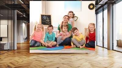 Kindergarten teacher with group of children in playroom. Indoor activity Wall mural