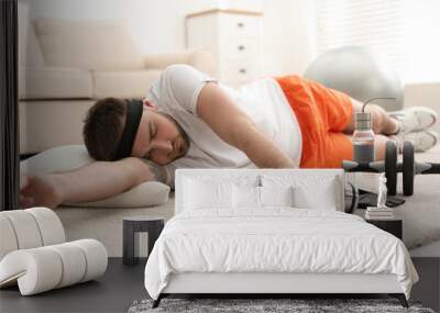 Lazy young man with sport equipment sleeping on floor at home Wall mural