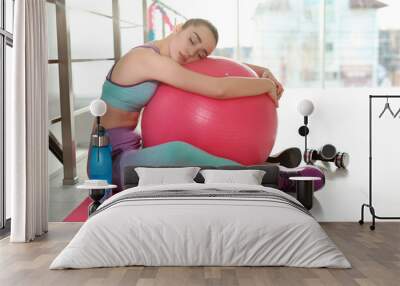 Lazy young woman with sport equipment on yoga mat indoors Wall mural