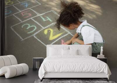 Little African American girl drawing hopscotch with chalk on asphalt outdoors. Happy childhood Wall mural