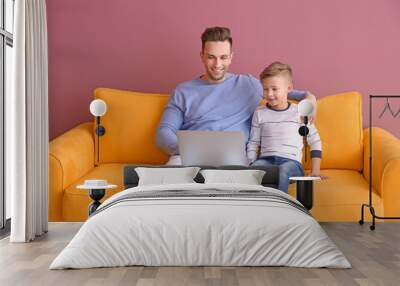 Little boy and his father with laptop sitting on sofa, indoors Wall mural