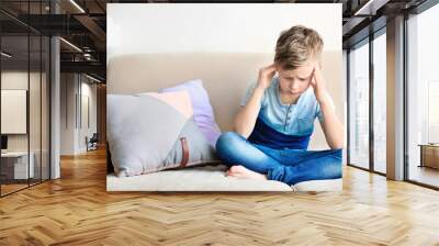 Little boy suffering from headache while sitting on couch at home Wall mural