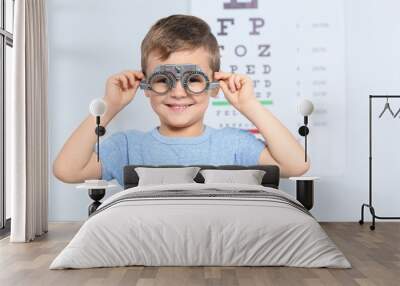 Little boy with trial frame near eye chart in hospital, space for text. Visiting children's doctor Wall mural