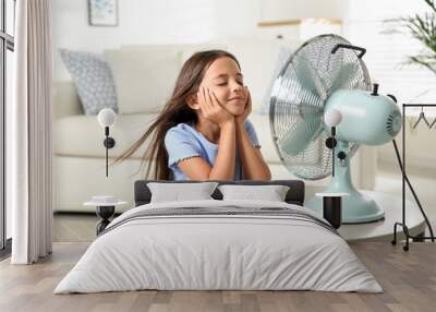 Little girl enjoying air flow from fan at home. Summer heat Wall mural