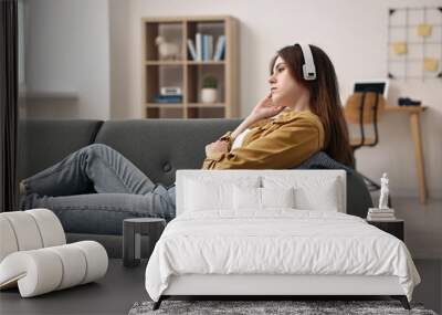 Loneliness concept. Sad teenage girl in headphones listening to music on sofa at home Wall mural