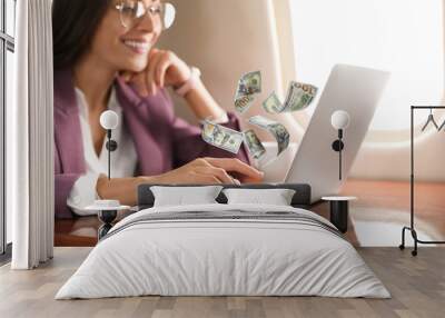 Making money online. Woman using laptop at table and flying dollars Wall mural