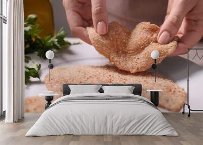 Making schnitzel. Woman putting slice of meat with bread crumbs onto plate at table, closeup Wall mural