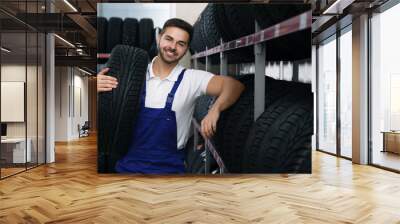 Male mechanic with car tire in auto store Wall mural