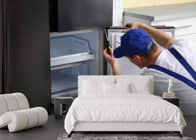 Male technician with screwdriver repairing refrigerator in kitchen Wall mural