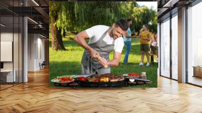 Man cooking meat and vegetables on barbecue grill in park Wall mural