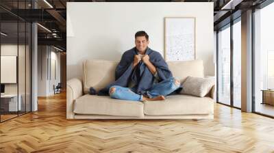 Man covered with warm dark blue plaid sitting on sofa at home Wall mural