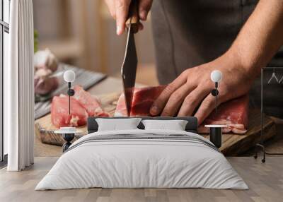 Man cutting fresh raw meat on table in kitchen, closeup Wall mural