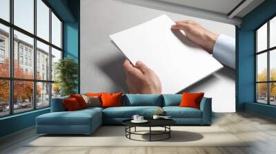 Man holding blank notebook at light grey table, closeup. Mockup for design Wall mural