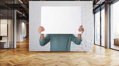 Man holding blank poster near white brick wall. Mockup for design Wall mural