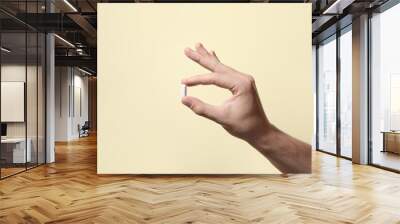 Man holding pill on beige background, closeup Wall mural