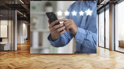 Man leaving service feedback with smartphone at home, closeup. Stars over device Wall mural