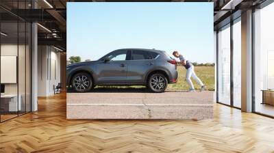 Man pushing broken car along country road Wall mural